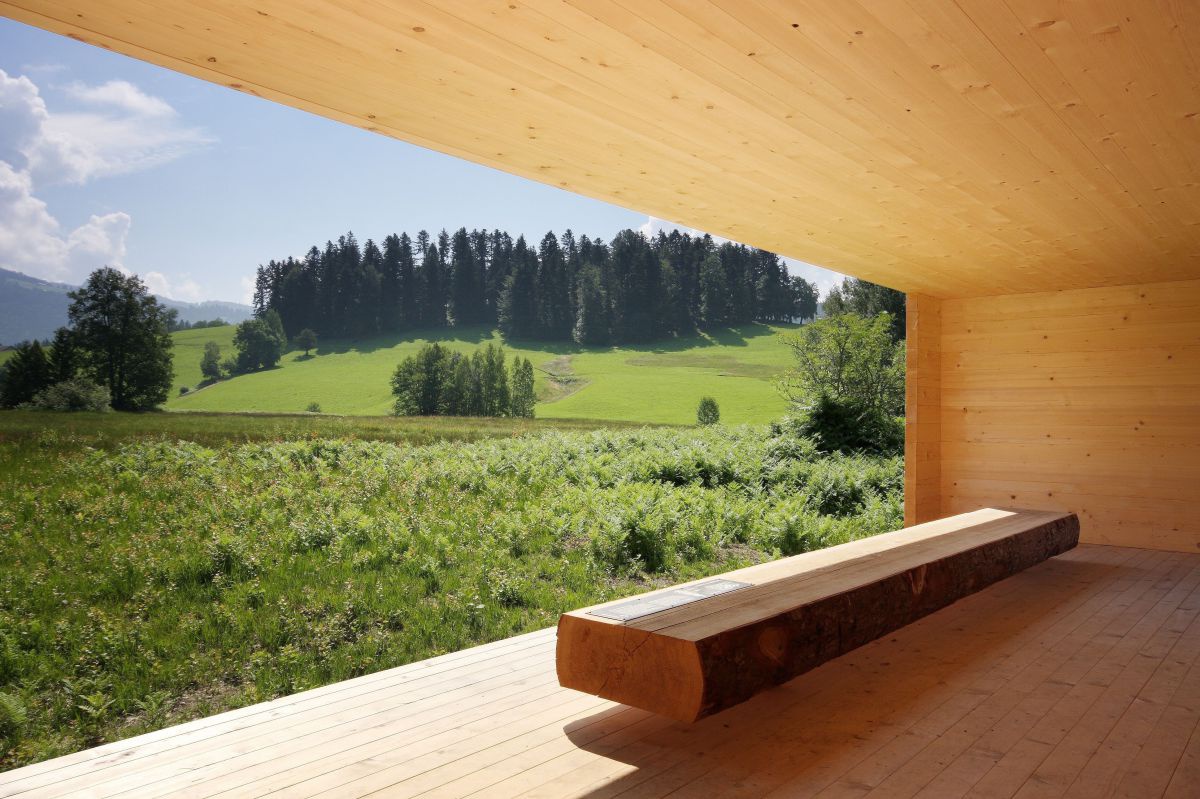 Aussichtsraum aus Holz mit Bank aus einem Holzstamm mir Aussicht auf die Landschaft.